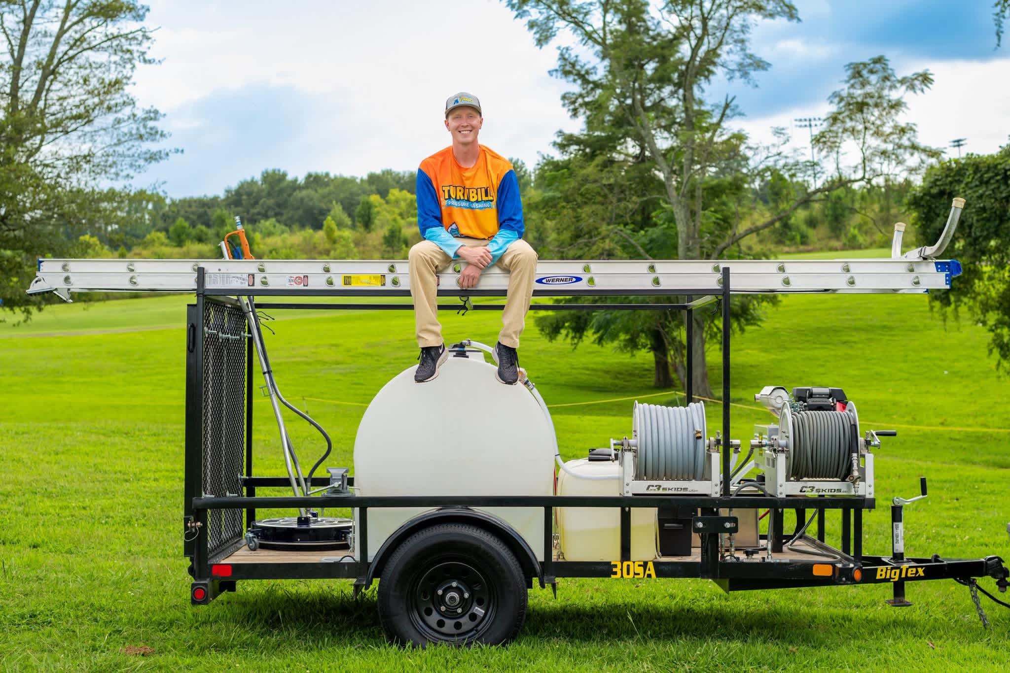 Jacob Turnbill sitting on ladder mounted on the pressure washing trailer of tools